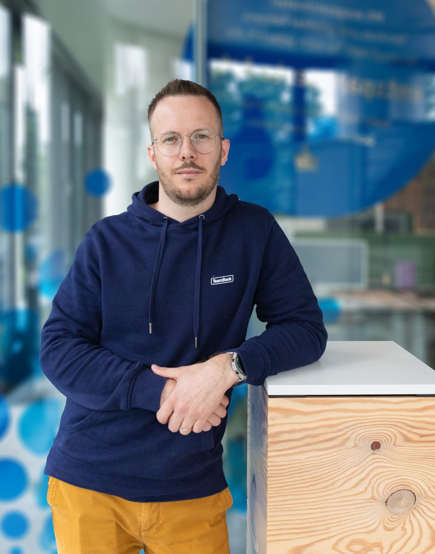 Mann in TeamBank-Hoodie lehnt sich an Pult an.