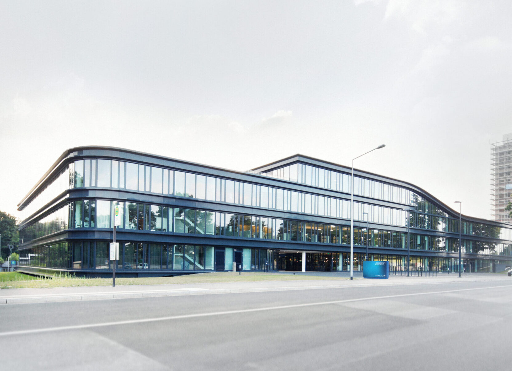 Das Gebäude der TeamBank in der Außenansicht. Wolkenverhangener Himmel. Drei Stockwerke, Glasfront, TeamBank Schild vor dem Eingang. Grünflächen außen herum.