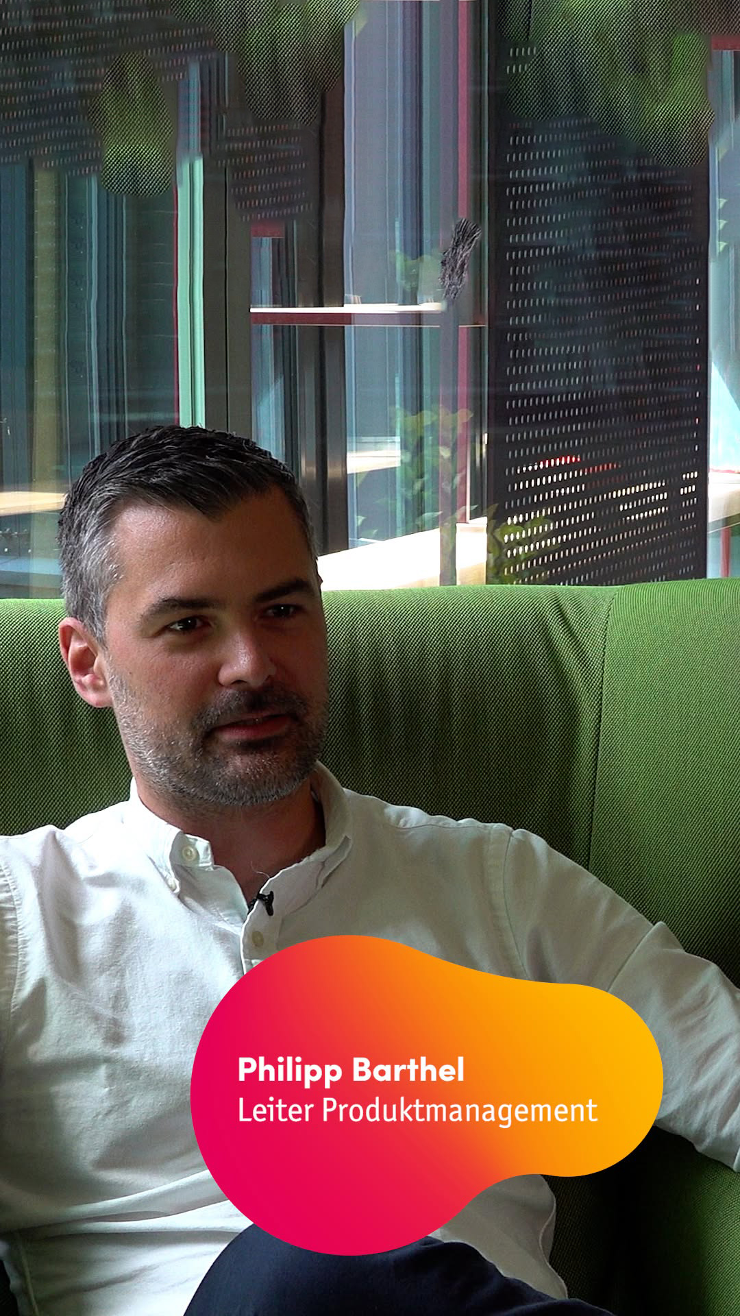 Philipp Barthel mit dunklen Haaren und Bart sitzt auf einem grünen Sessel und schaut leicht an der Kamera vorbei. Bauchbinde: Philipp Barthel - Leiter Produktmanagement.