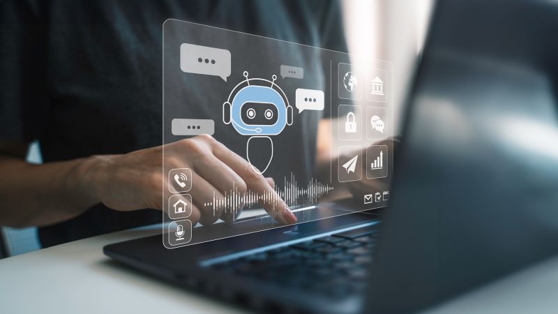 Eine Person tippt auf einem Laptop. Über dem Bildschirm ist eine transparente Benutzeroberfläche mit einem Chatbot-Symbol, Sprechblasen, Icons und Tonwellen eingeblendet, die eine digitale Interaktion darstellen.