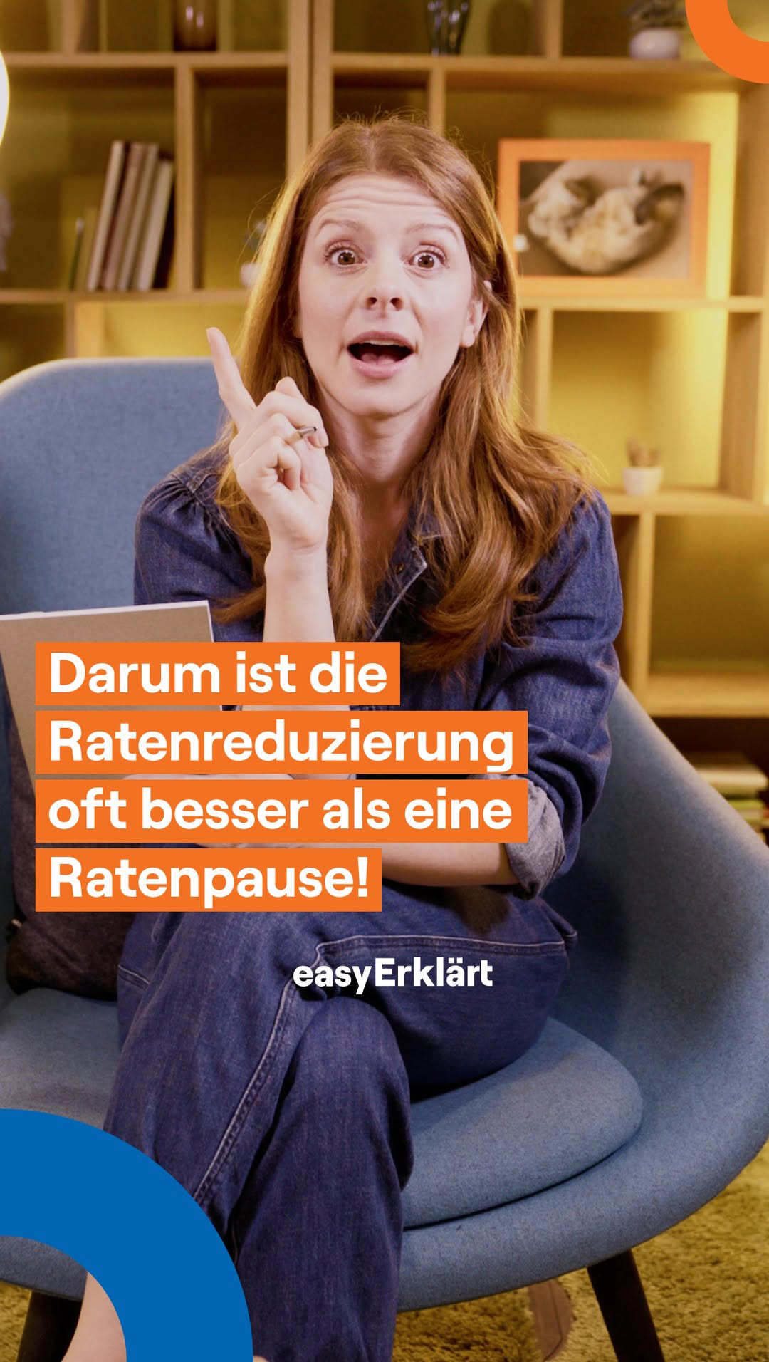 Junge Frau sitzt auf einem blauen Sessel, hat den Mund geöffnet und den Zeigefinger erhoben. Text liest sich: Darum ist die Ratenreduzierung oft besser als eine Ratenpause! easyErklärt